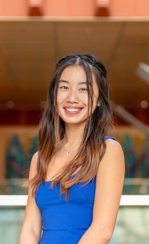 Person with long hair, in a blue dress, smiling at the camera