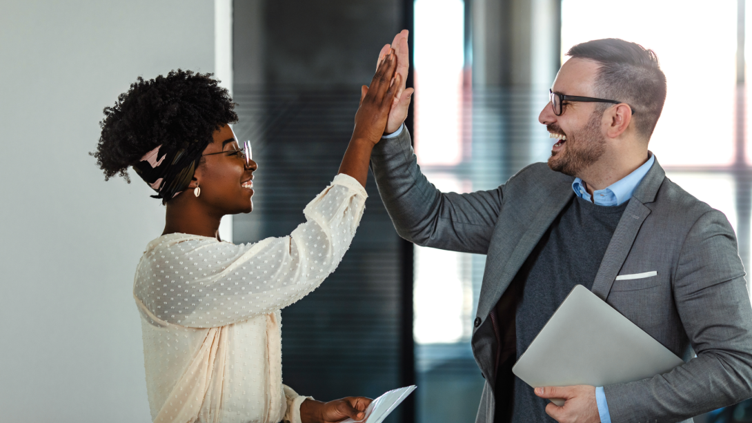 Coworkers celebrating achievement at office. Celebrating success. Happy young man standing in office and giving high five to his colleagues. Two business people high-five. Job well done